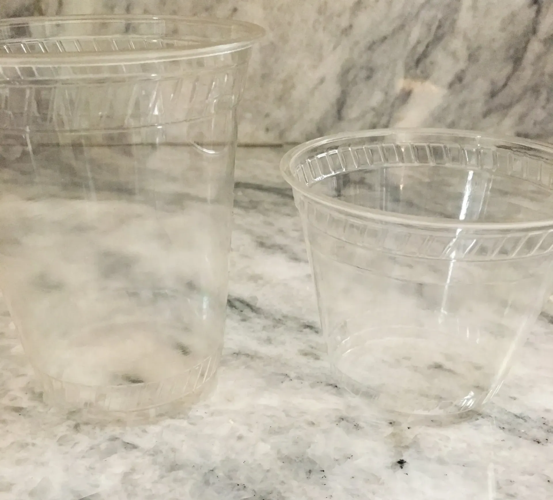 Two clear plastic cups on a white marble countertop with a gray marble backsplash