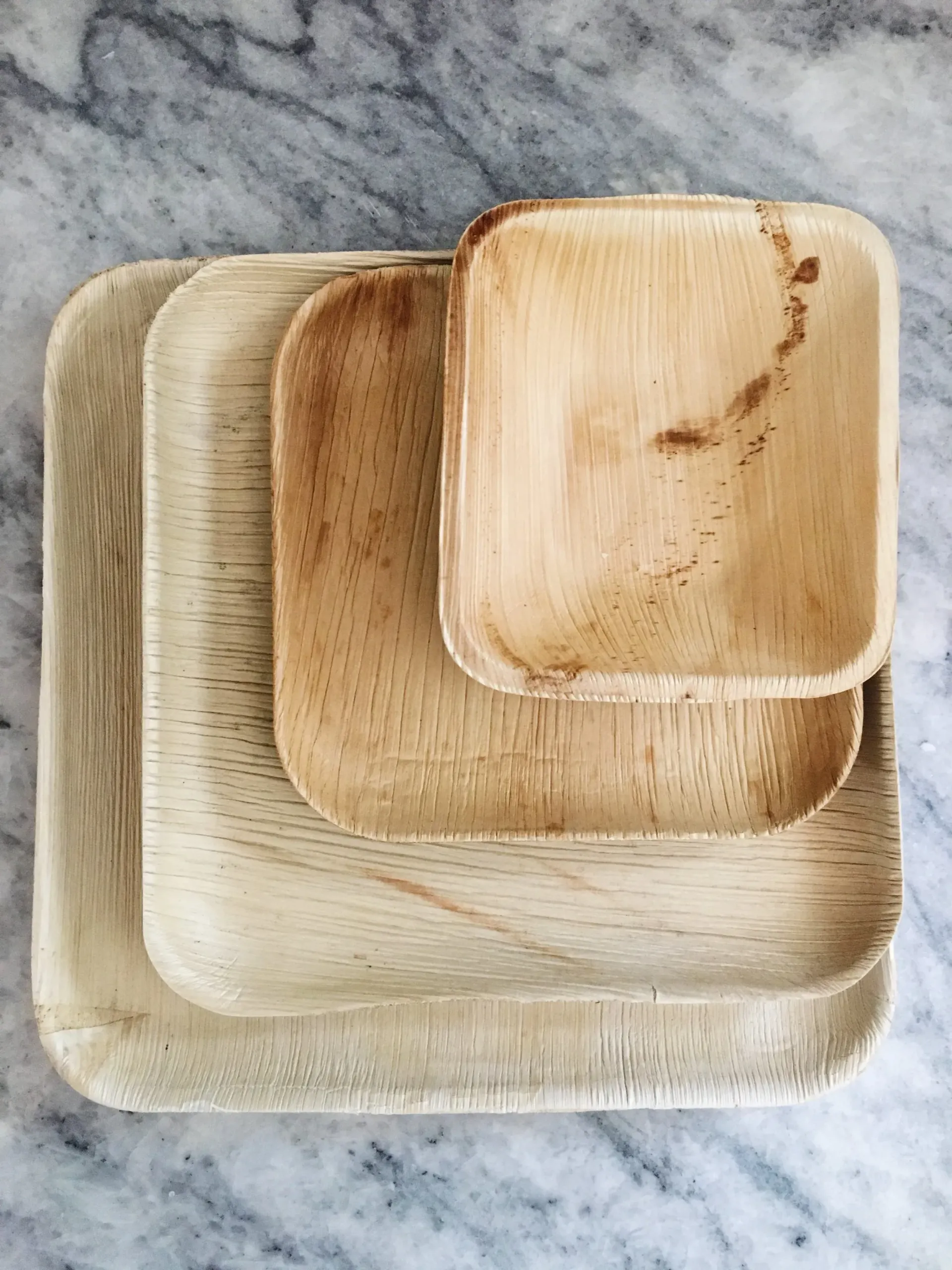 Three stacked square wooden trays on a light marble surface