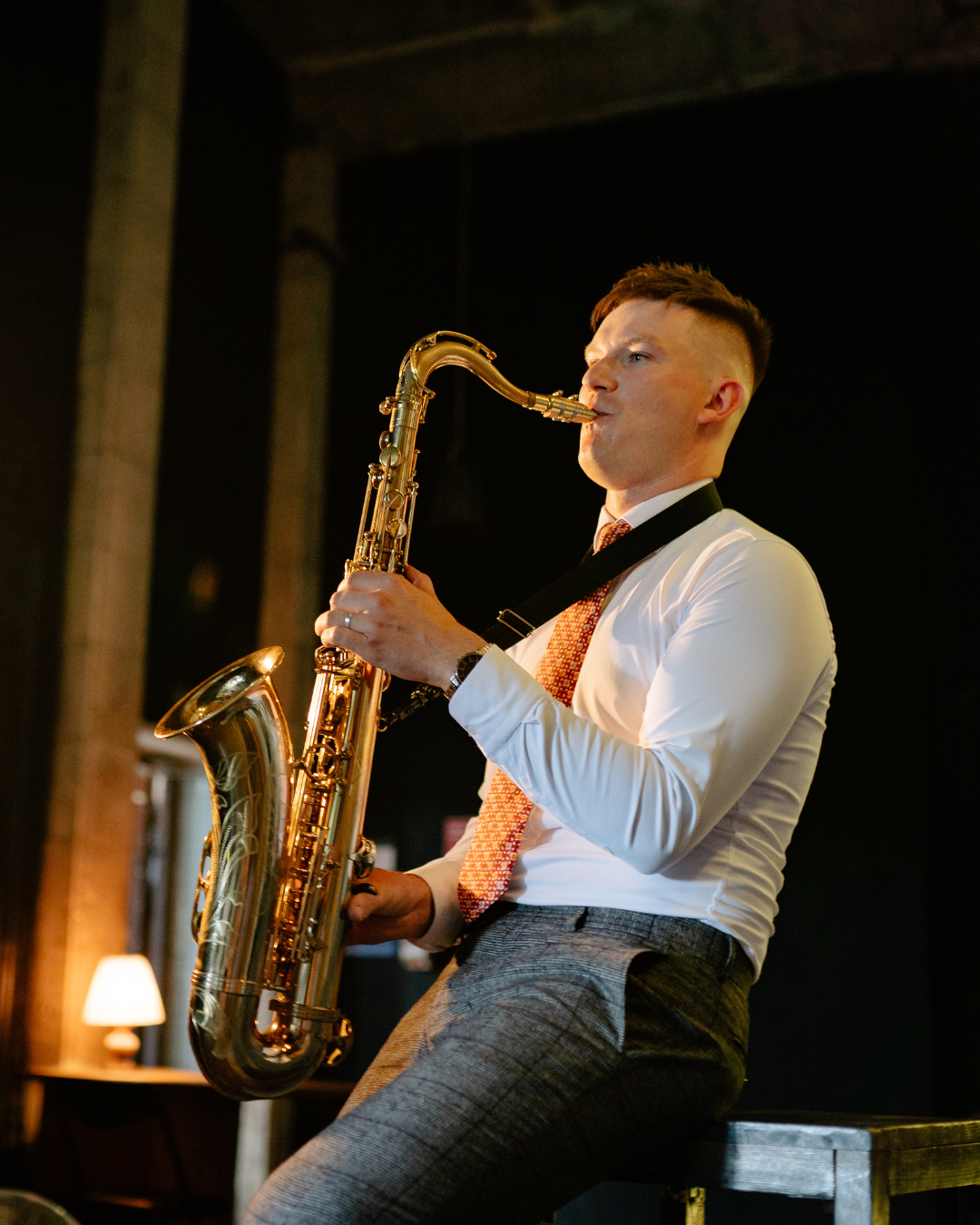 Saxophonist performing on stage with a gold saxophone, seated under warm spotlight