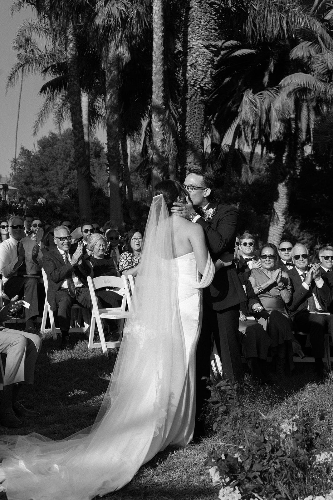 Bride and groom kiss at an outdoor wedding ceremony with guests seated nearby