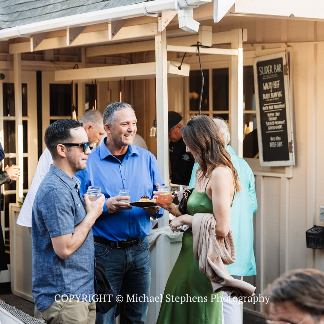 Three adults chatting with drinks outside a café patio under a wooden awning