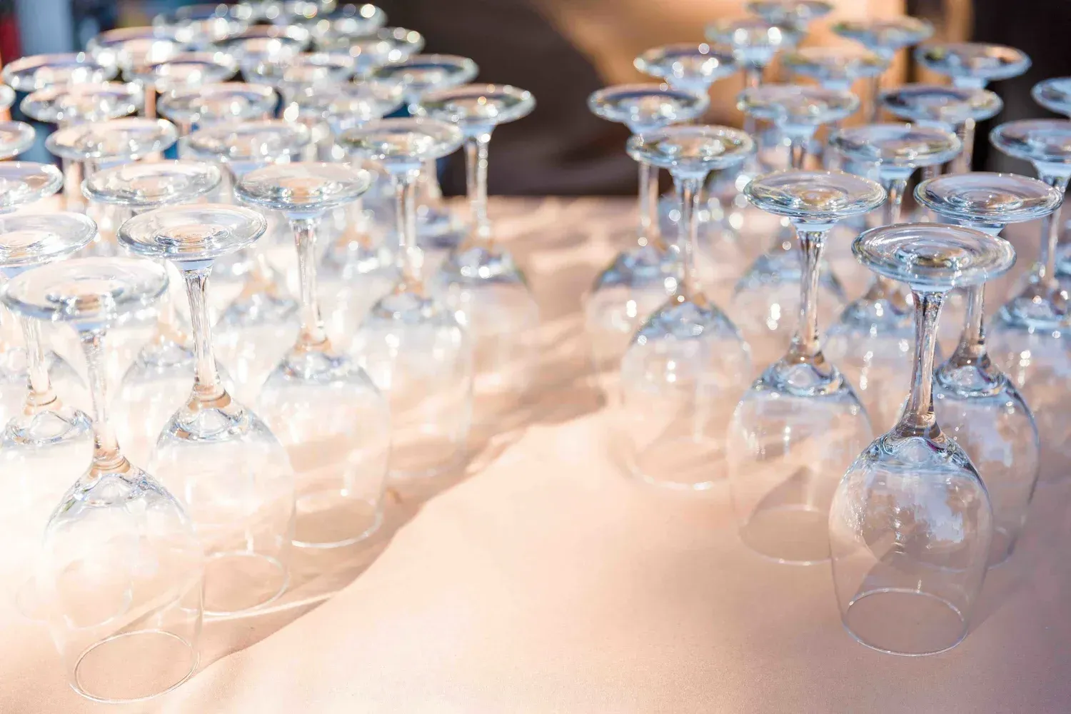 Rows of upside-down wine glasses on a white tablecloth, lit with warm reflections
