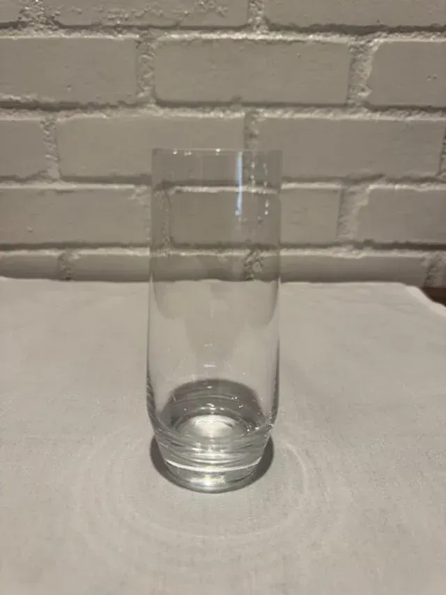 Empty clear glass on a white table against a white brick wall background