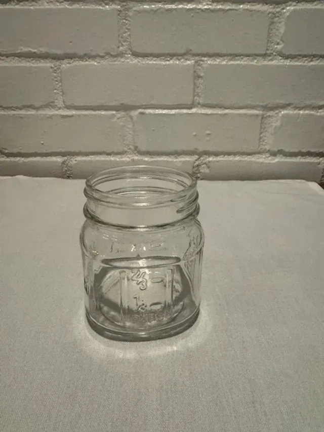Clear glass mason jar on a white surface in front of a gray brick wall.