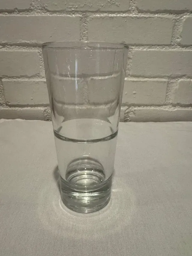 Empty clear drinking glass on a white surface against a white brick wall.
