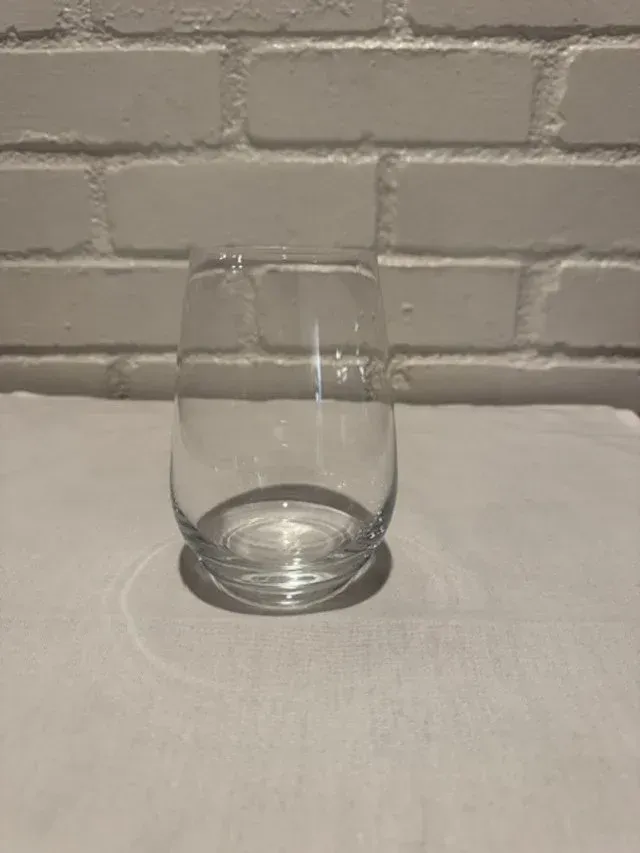 Empty clear glass on a white table against a white brick wall.
