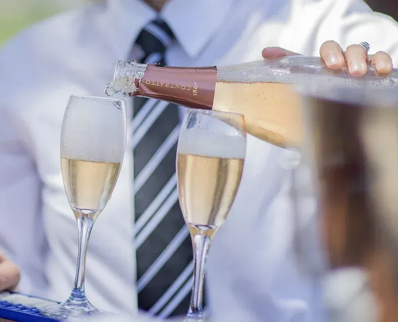 Champagne being poured into glasses at a formal celebration, with a person in a white shirt and tie in the background