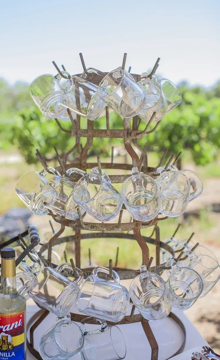 Clear glass mugs stacked on a tiered stand outdoors, with a blurred garden background.