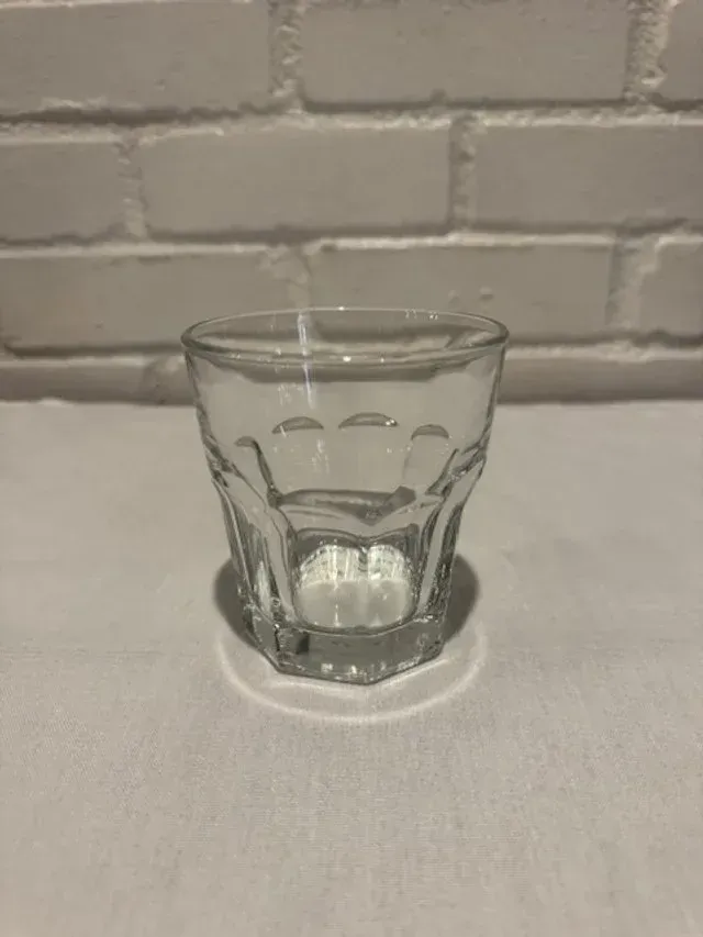 Clear faceted glass on a white surface against a white brick wall.