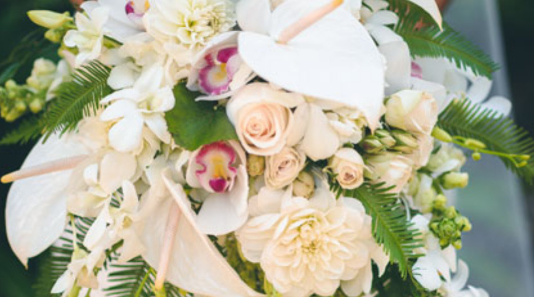 Cream and white floral bouquet with roses and orchids, accented by green foliage and ribbon