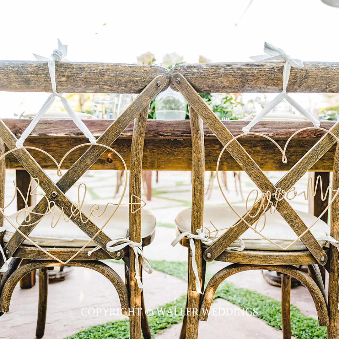 Two wicker chairs at a rustic wooden table on a balcony with rope railing and bright outdoor view