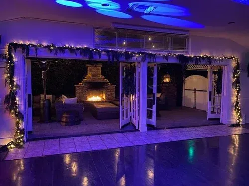 Decorated indoor patio with string lights, blue lighting, and a lit fireplace under a covered structure