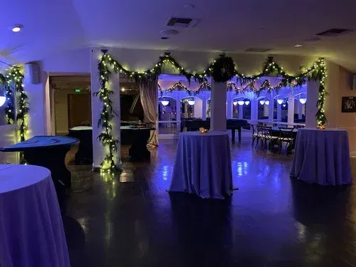 Decorated banquet hall with purple lighting, garland-wrapped archways, and round tables draped in purple cloths