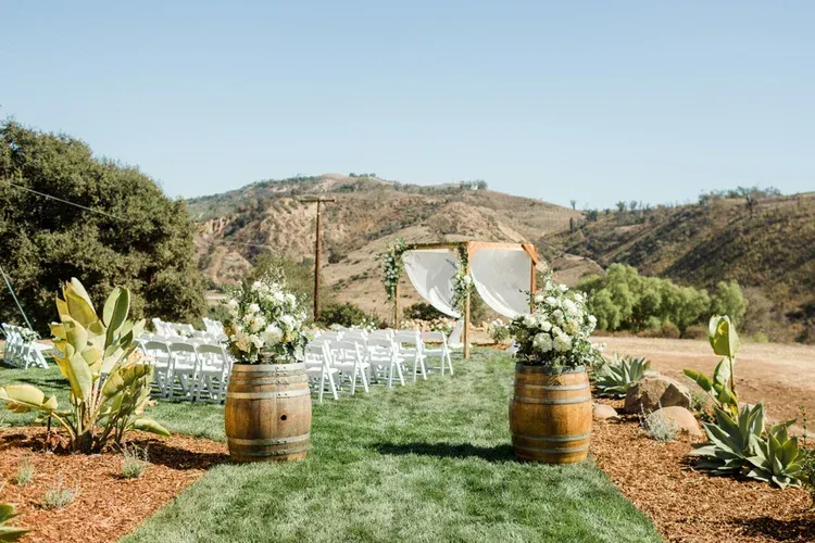 Outdoor wedding aisle with white chairs, floral arch, and barrel decor set against a mountain backdrop