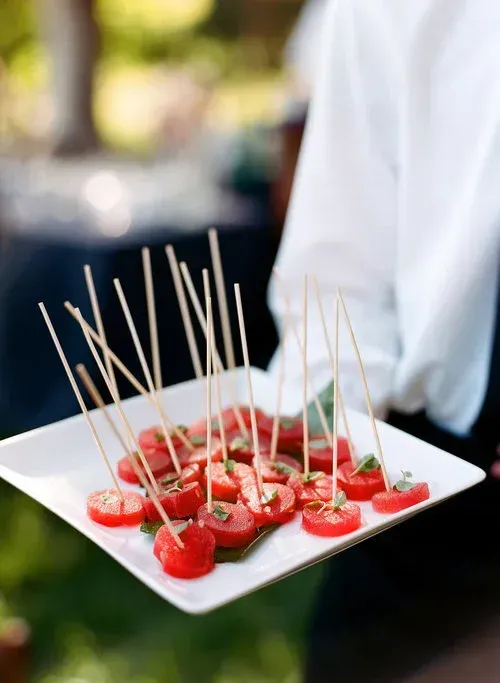 Skewers of cherry tomatoes and mozzarella on a white tray at an outdoor event