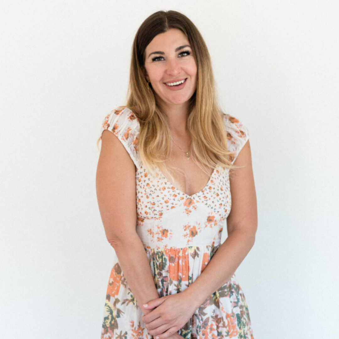 Smiling woman in a white floral dress standing against a plain white background