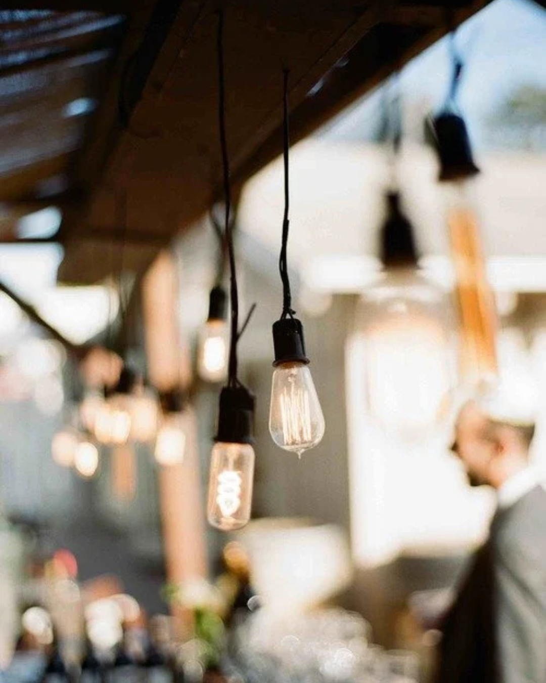 Warm café interior with hanging Edison bulbs and soft bokeh lights, blurred patrons in the background