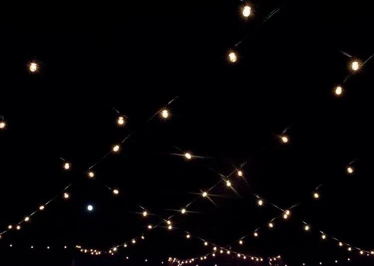 Warm string lights crisscross against a dark night sky, with small glowing bulbs in the distance.