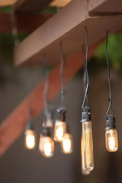 Warm hanging Edison bulbs glowing under a wooden beam outdoors