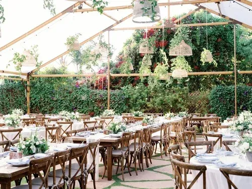 Outdoor dining area with wooden tables and chairs under a canopy, surrounded by lush greenery