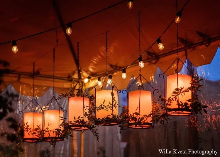 Warm hanging lanterns and string lights under an orange tent at an outdoor evening event