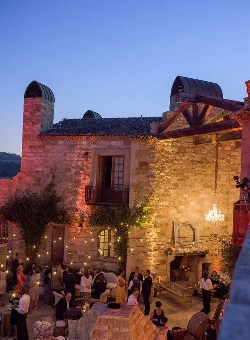 Outdoor evening gathering at a stone courtyard lit with warm lights under a blue sky