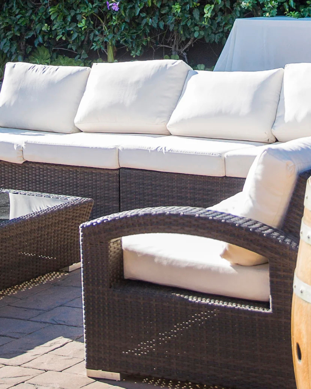 White-cushioned wicker outdoor sofa and armchair on a patio in sunlight
