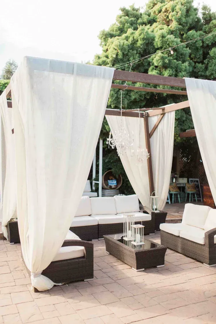 White draped cabana seating area with cushioned benches and wooden tables on a patio outdoors