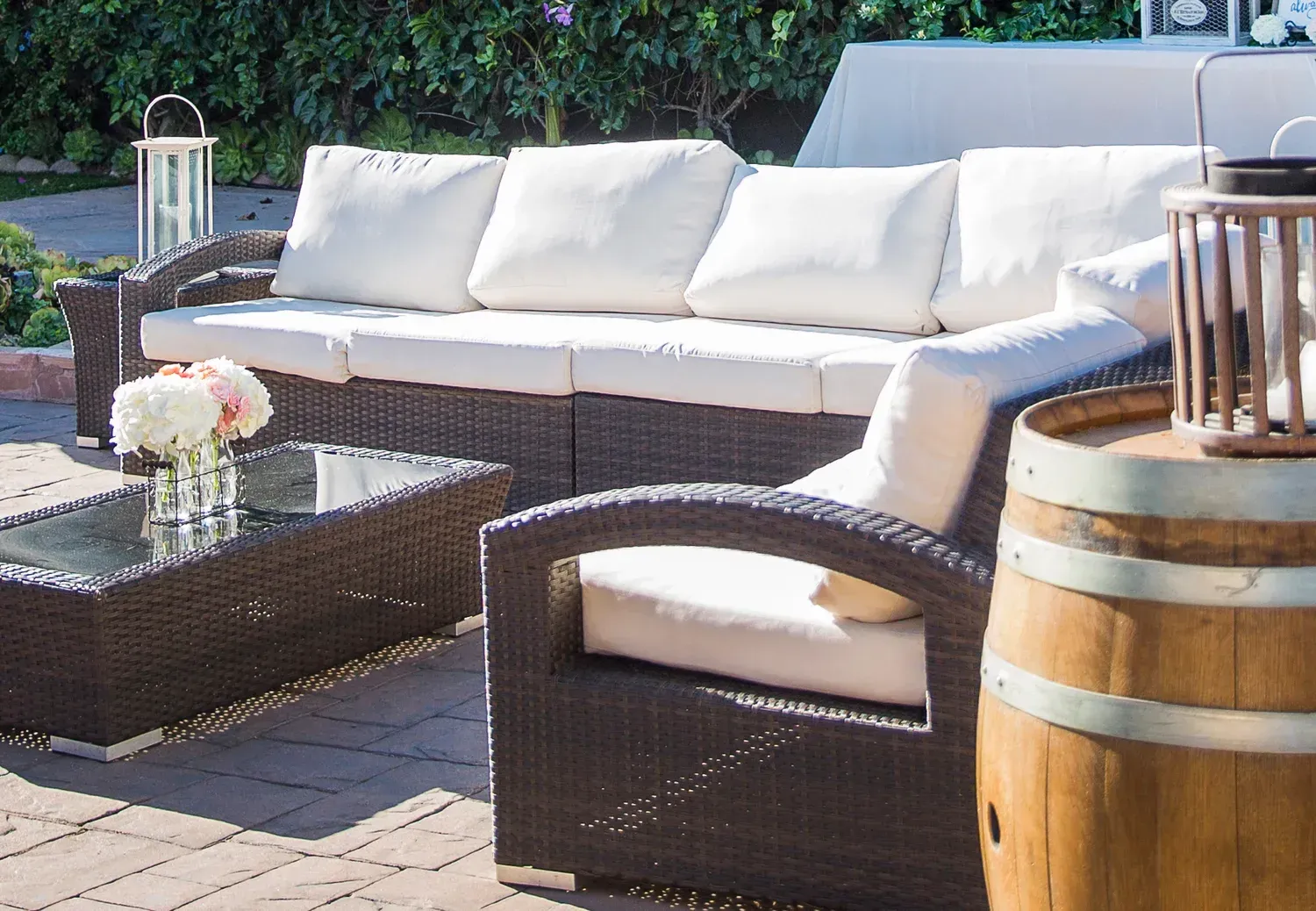 Outdoor patio with wicker sofa, white cushions, glass coffee table, and wooden barrel side table