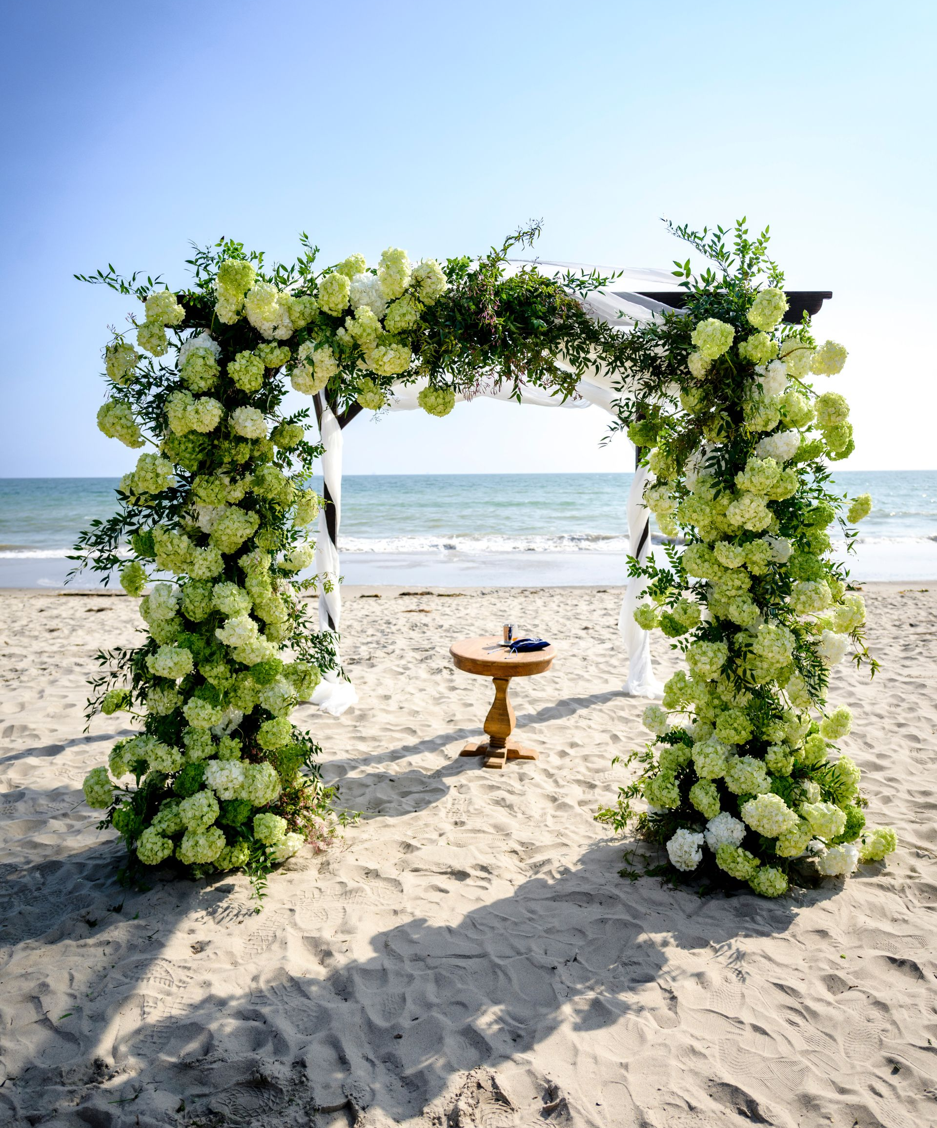 Flower-covered beach arch with a small table on the sand by the ocean