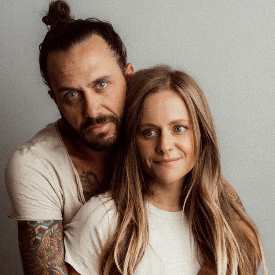 Two people posing closely indoors, both in white tops, with calm expressions.