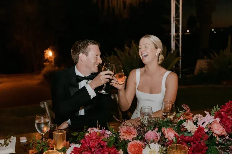 Couple in formal wear toasting at a candlelit dinner with colorful flowers at the table