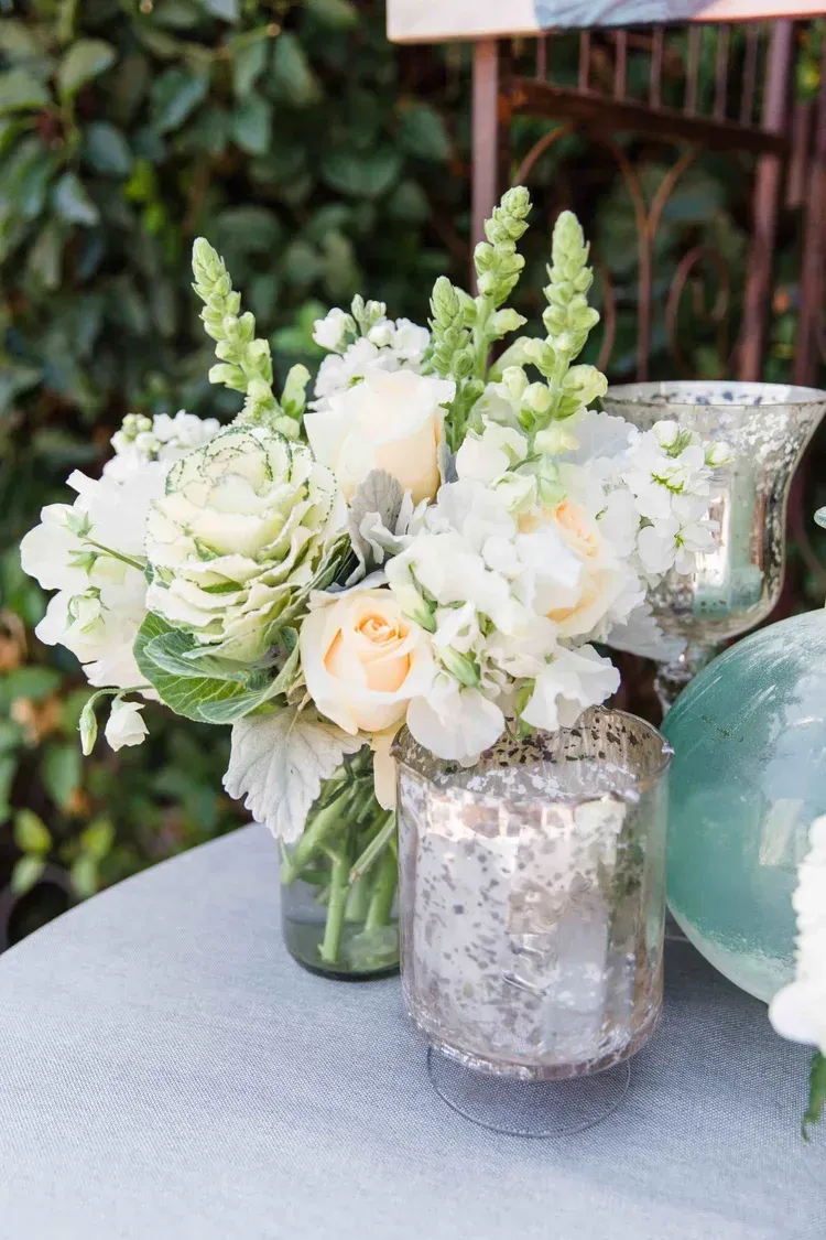 White and blush floral arrangement in rustic glass vases on a textured outdoor table