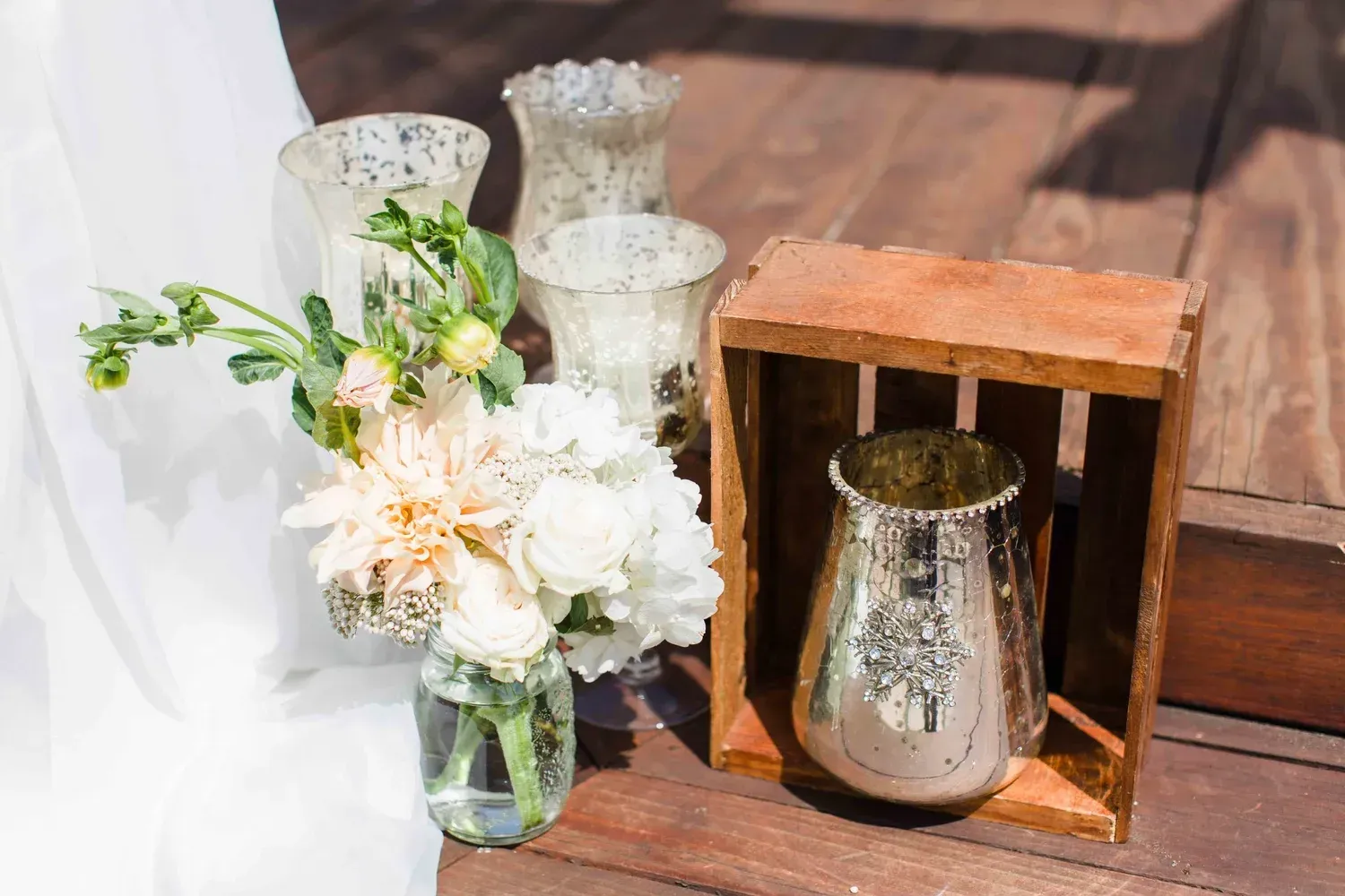 White floral bouquet in glass vase beside candle holders and a rustic wooden lantern on a sunlit floor