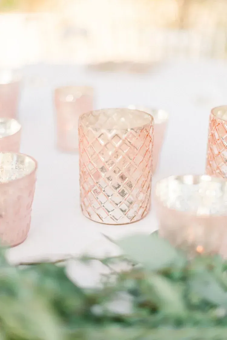 Pink glass votives on a softly lit table with blurred white and green floral decor