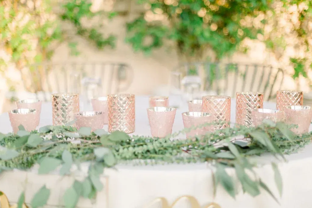 Pastel pink and gold party table with glassware and greenery centerpiece outdoors