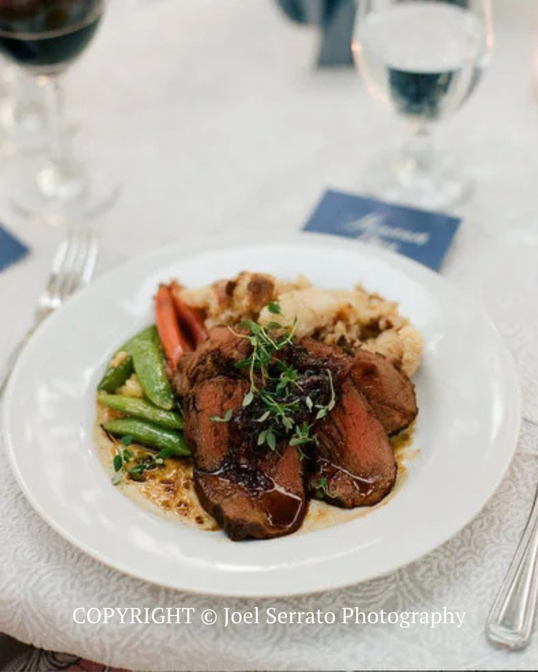 Plated roast meat with green beans and rice on a white tablecloth at a formal dinner table