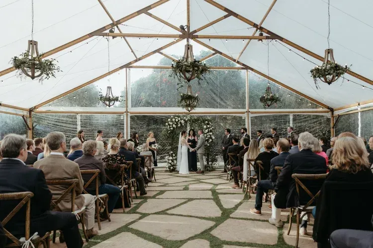 Wedding ceremony in a glass greenhouse with guests seated in rows facing the couple at the altar
