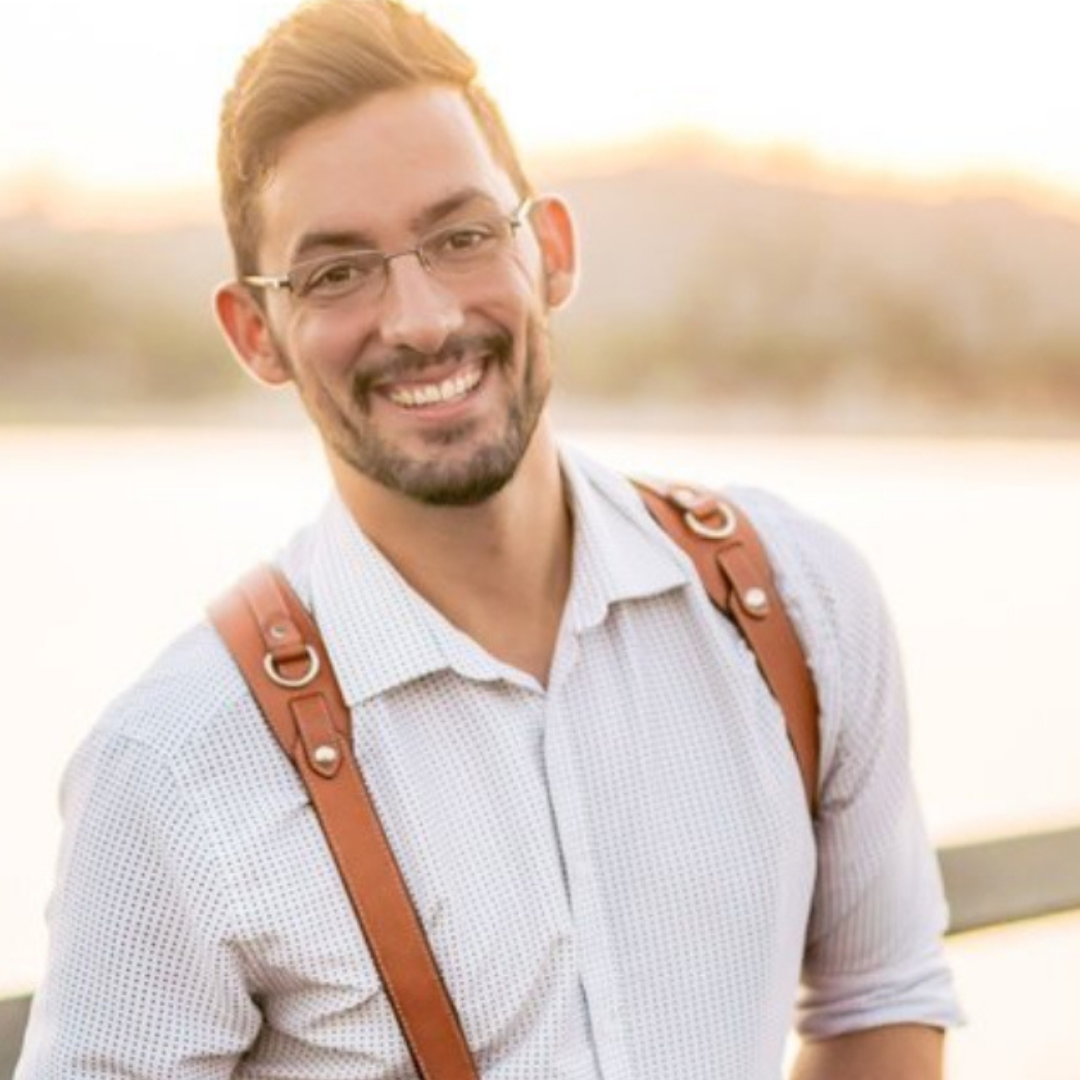 Smiling man with glasses and leather suspenders outdoors in warm sunset light