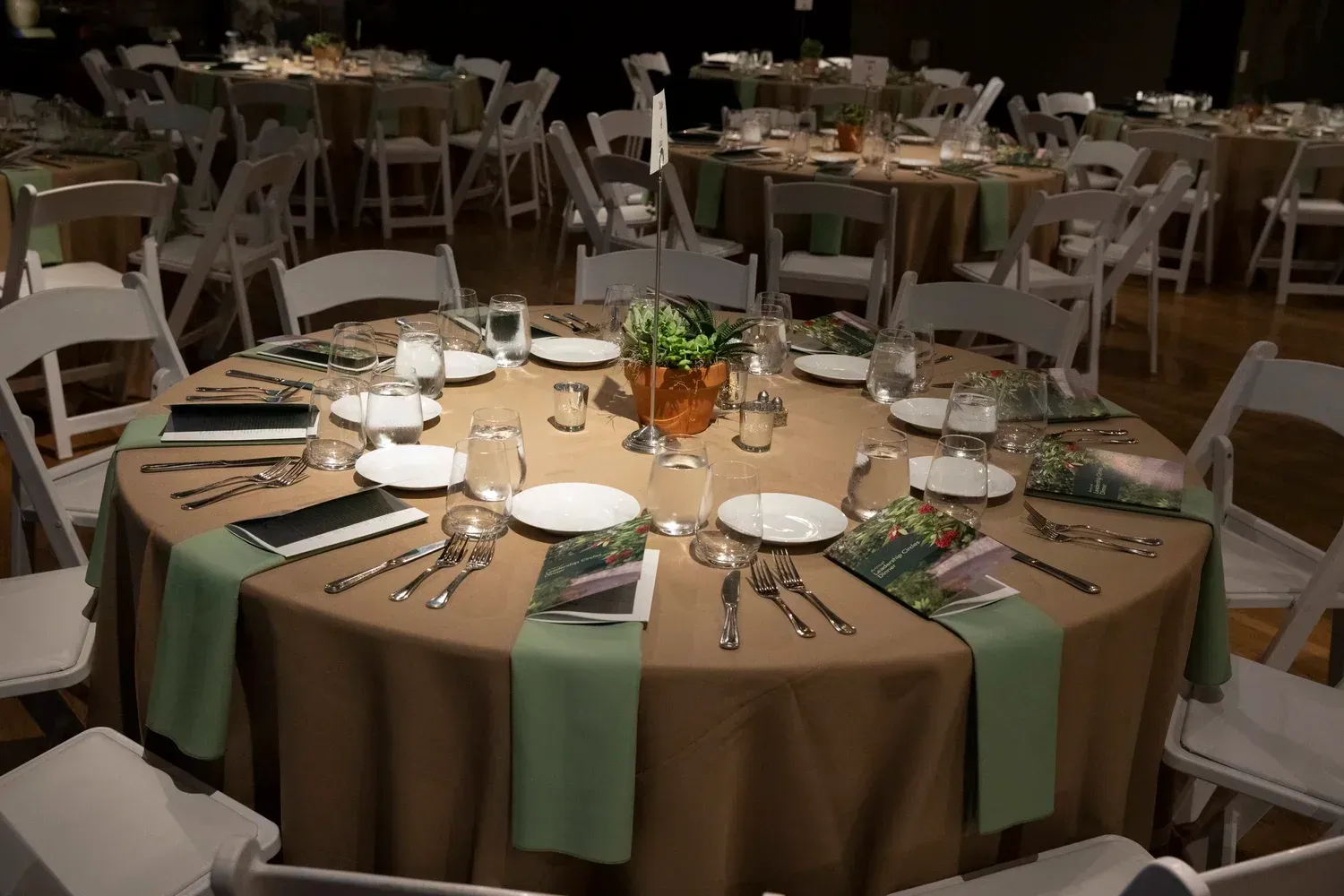 Round banquet table set with plates, utensils, candles, and flowers in a dimly lit event hall