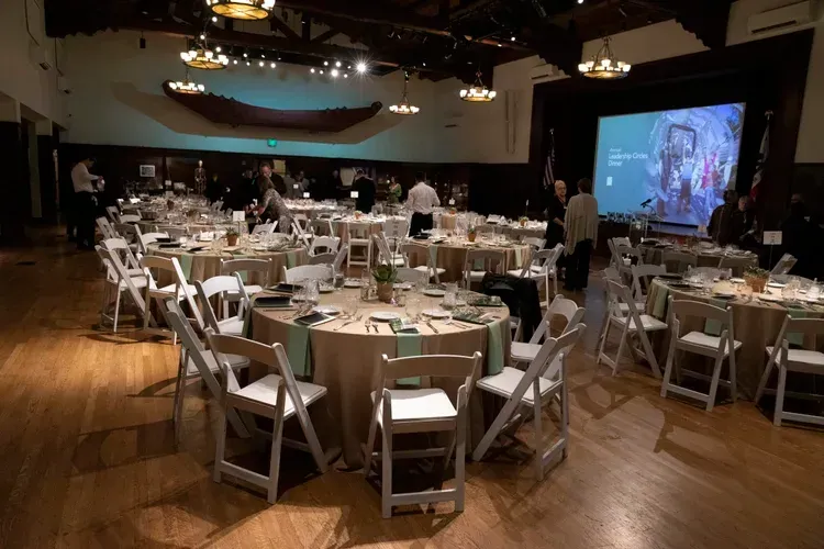 Banquet hall with round tables, white chairs, and a projector screen during an event setup