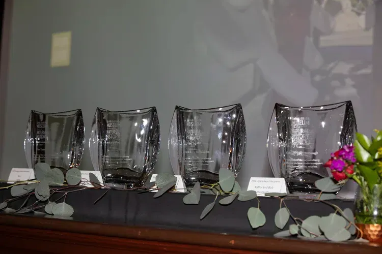 Four clear glass candle holders with leaves and flowers arranged on a table against a gray wall.