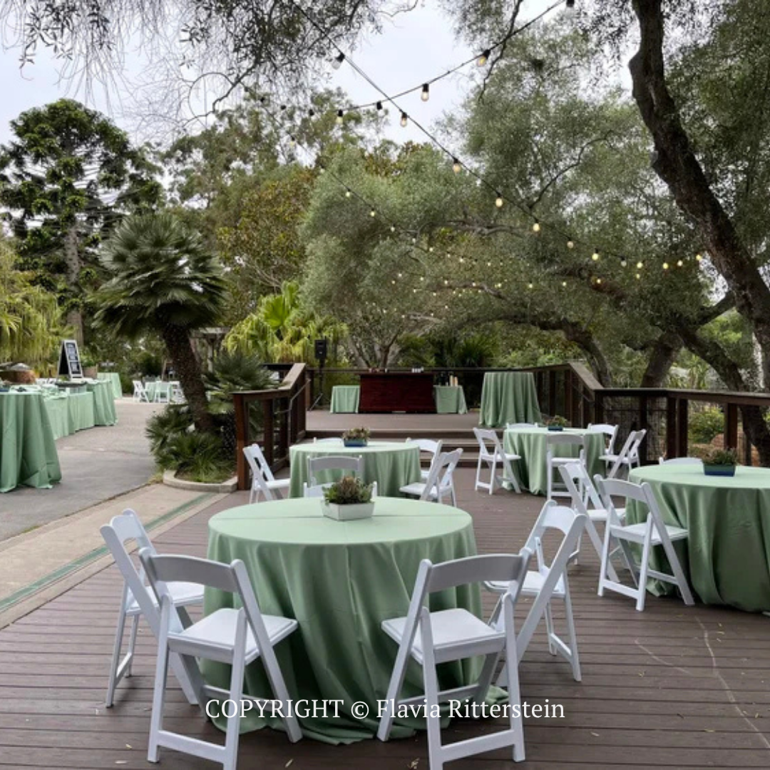 Outdoor patio with mint-green tablecloths and white chairs under trees, set for an event