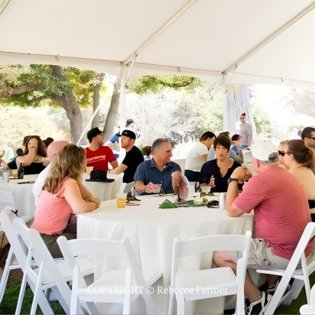 People seated at round tables under a white event tent, chatting and eating