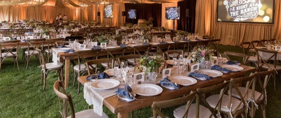 Elegant banquet setup with long tables, white dishes, and warm amber drapes on a grass floor