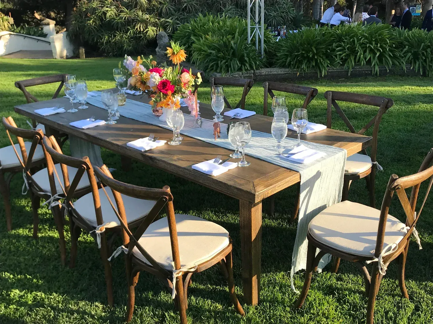 Outdoor dining table set with white chairs, flowers, and table settings in a garden.