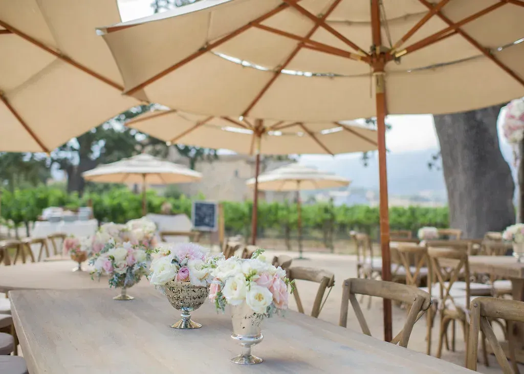 Outdoor reception tables with beige umbrellas and pastel floral centerpieces in a garden setting