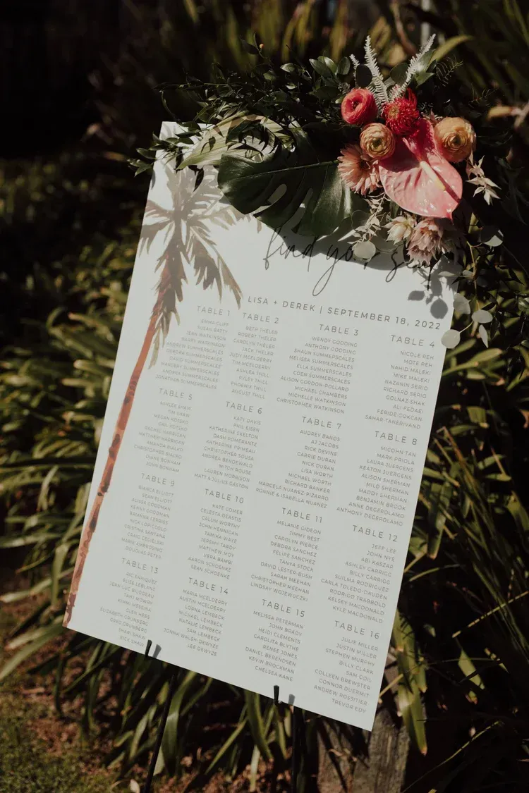 A holiday wreath with red flowers and a white printed sheet pinned to it outdoors.