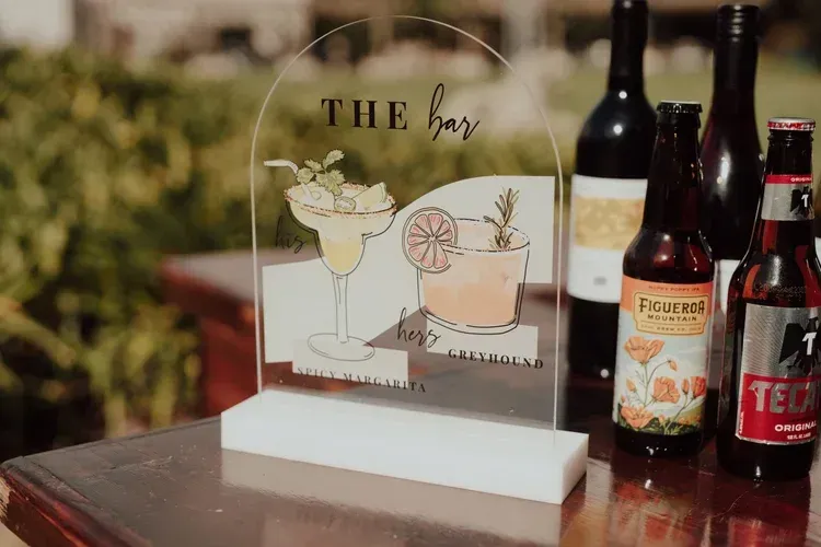 Event sign reading “THE bar” beside cocktail bottles on a table outdoors
