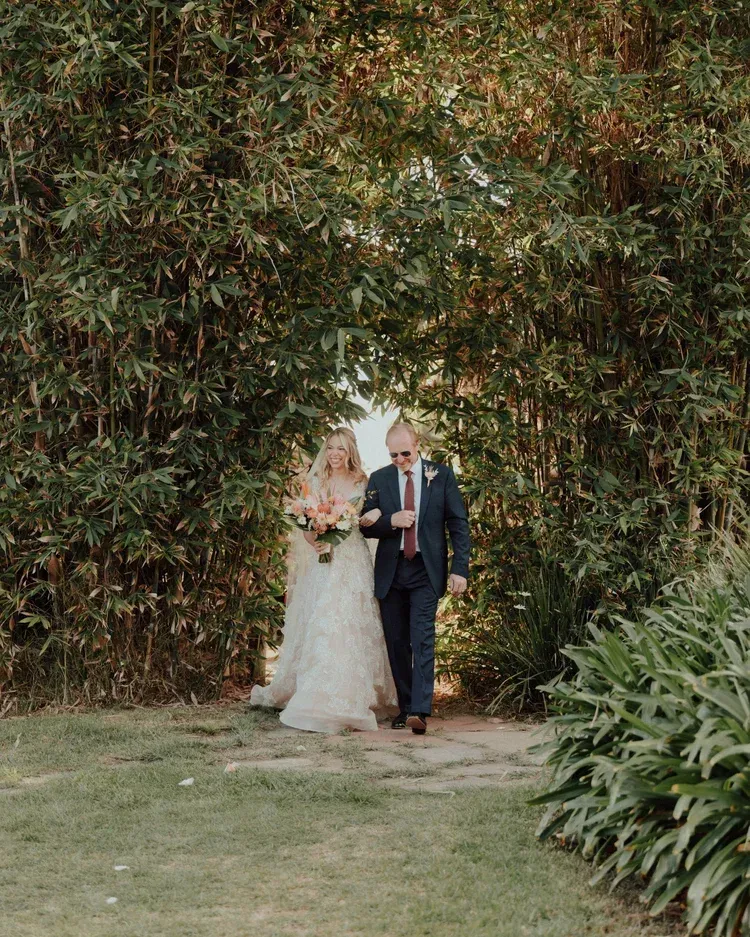 Bride and groom walking hand in hand through a leafy garden archway
